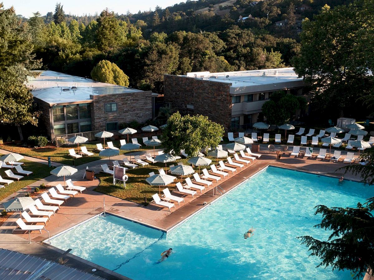 This image shows an outdoor swimming pool area with lounge chairs and umbrellas, surrounded by trees and buildings in the background.