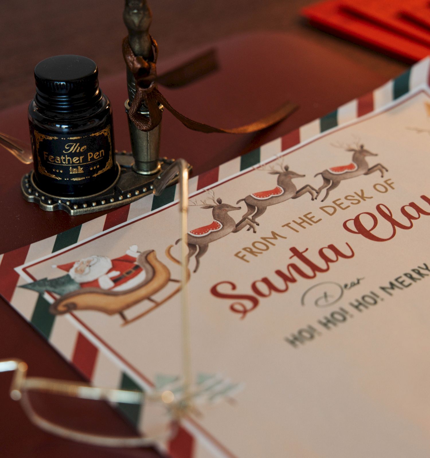 A whimsical &ldquo;From the Desk of Santa Claus&rdquo; letter, featuring reindeer and sleigh illustrations, an ink bottle, pen, and reading glasses.