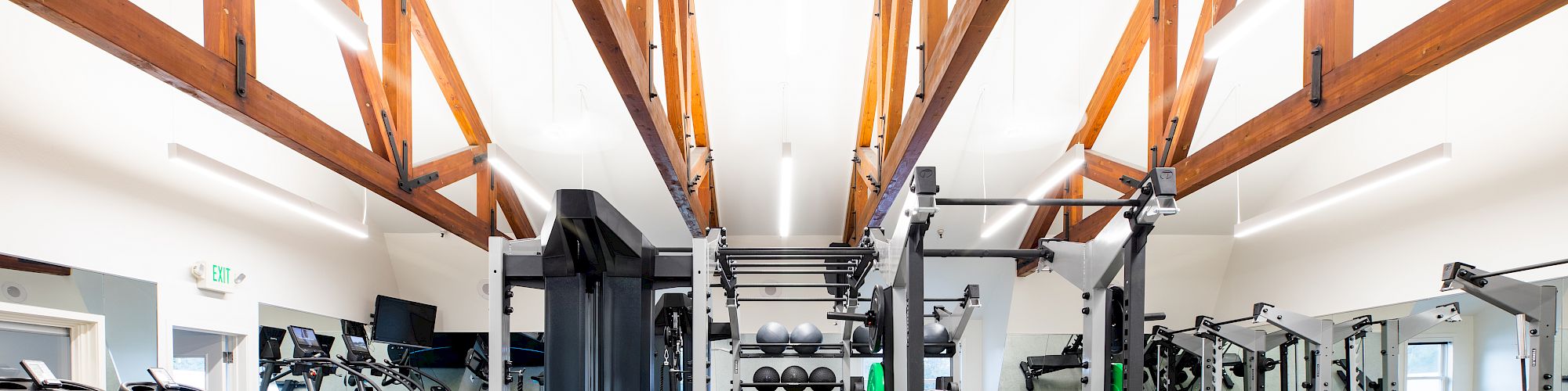 This image shows a modern gym with various workout equipment, including treadmills, weight machines, benches, and dumbbells, in a well-lit space.